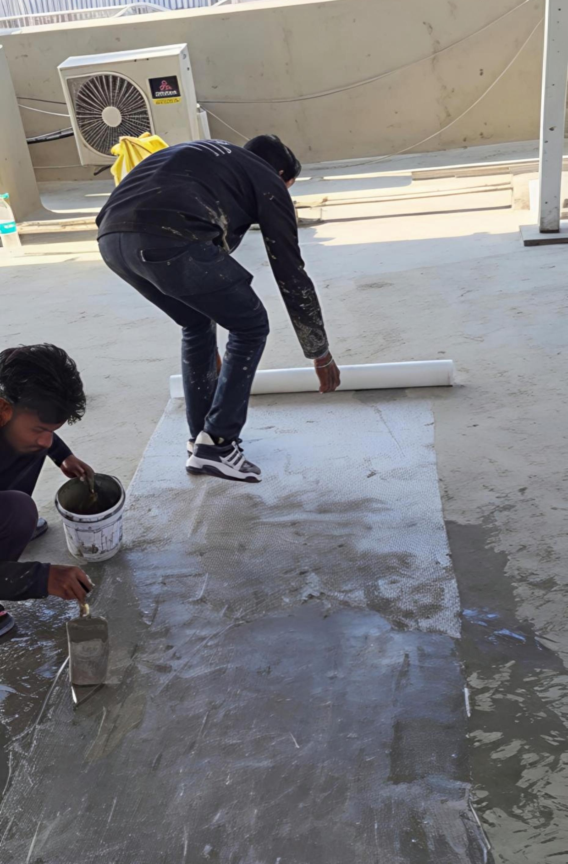 Worker laying fiber mesh reinforcement into the 5-layer waterproofing system on a Noida roof.