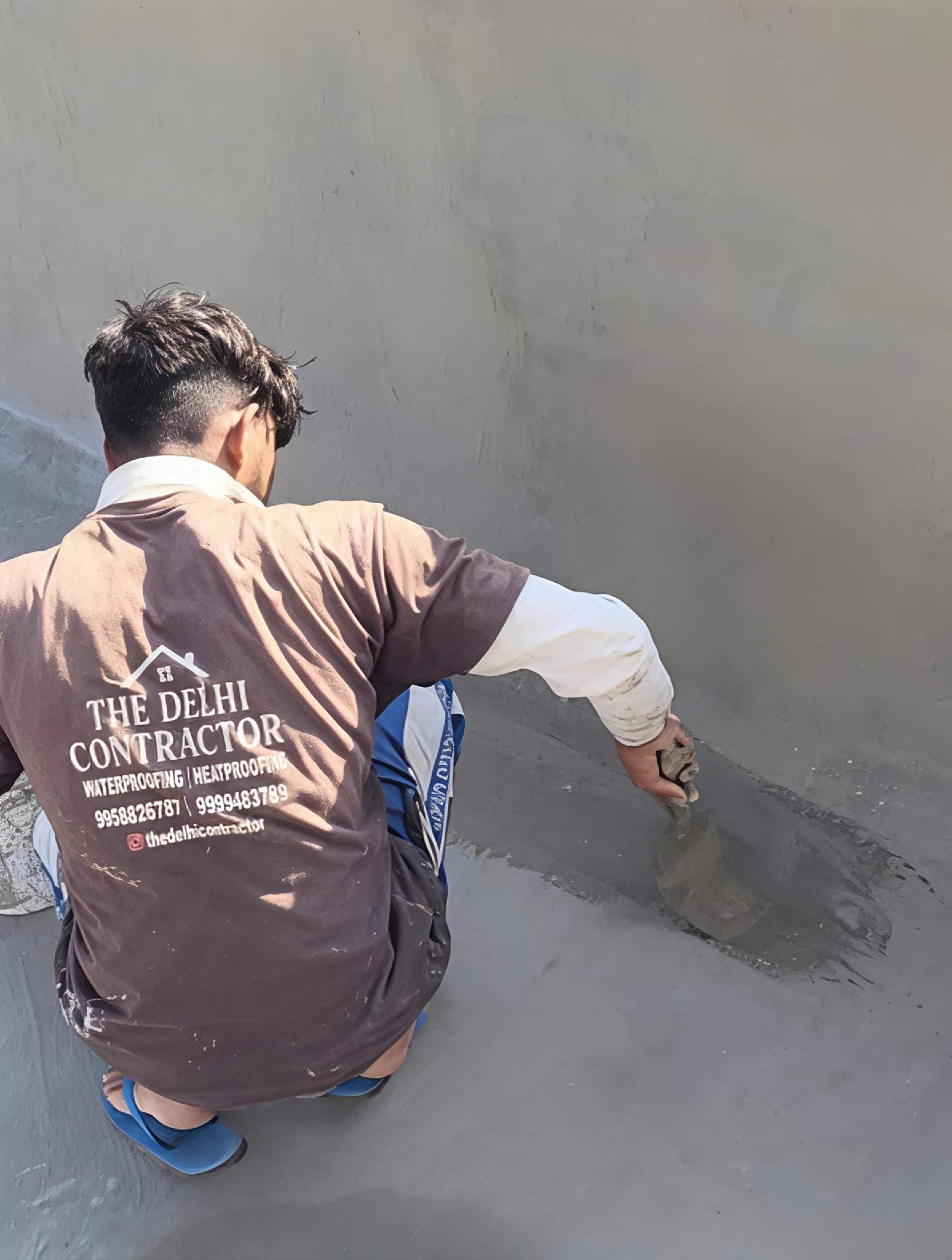 Crew member in a branded shirt applying the 5-layer waterproofing system on a rooftop in Ashok Vihar, Delhi.