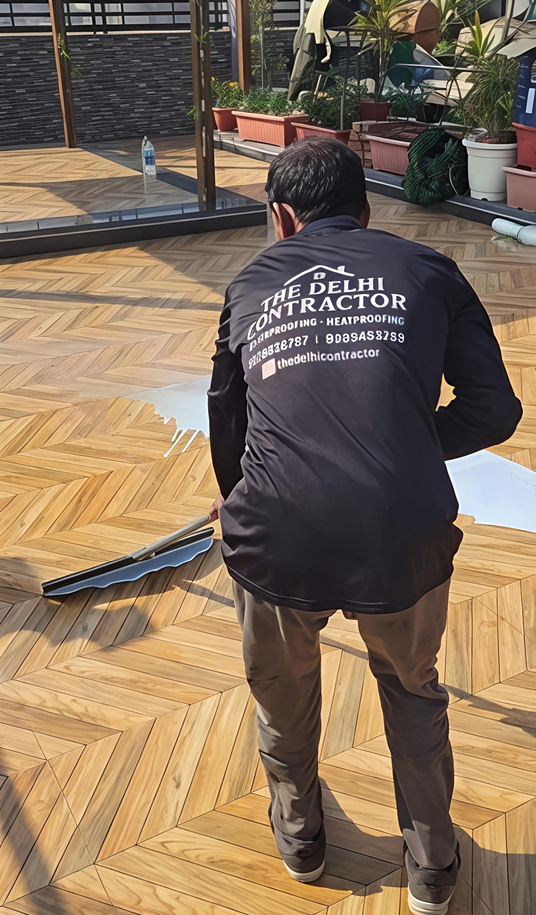 Applicator in a branded The Delhi Contractor shirt rolling transparent 5-layer waterproofing onto a tiled terrace in Vasant Kunj, Delhi.